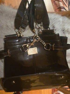 Brun handväska från Dolce & Gabbana - Säljer en brun handväska från Dolce & Gabbana i glansigt skinn med detaljer i krokopräglat läder. Väskan har metallkedjor, flera innerfack med dragkedja och breda handtag. Perfekt för dig som vill ha en lyxig och rymlig väska med snygga detaljer.