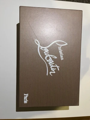 Svarta Christian Louboutin sneakers med nitar - Säljer ett par svarta sneakers från Christian Louboutin i mocka med ikoniska röda sulor och svarta spikar på tån. Skorna har snörning och en clean look.