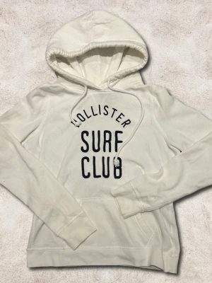 Hollister hoodie XS-S - En snygg hoodie från hollister i färgen vit. Storlek XS-S även fast det står M. En liten blå fäck på axeln som knappt syns när man bär den. Går nog bort i tvätten men kan ej garantera något. 