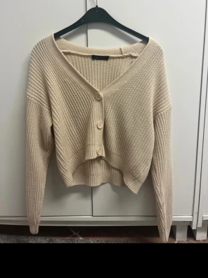 Beige croppad kofta  - Säljer en beige, croppad kofta från LCW Casual. Tröjan är stickad med grov ribbad struktur, har v-ringning och tre stora knappar framtill. Långärmad modell som passar perfekt till lager på lager under höst och vår.