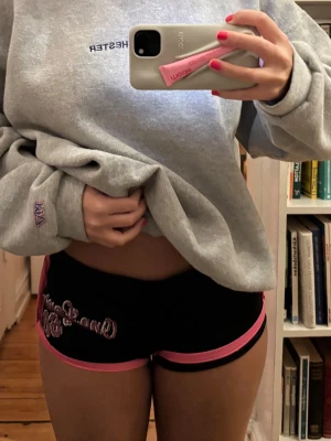 Svarta meshshorts med rosa detaljer - Säljer ett par svarta meshshorts med jamaica skriver där bak och  med rosa kanter och texten 'One Love 62'. Shortsen har låg midja.