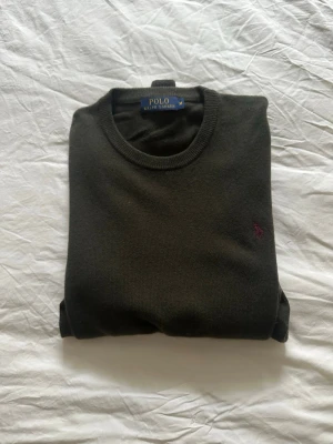 Mörkgrön stickad tröja Polo Ralph Lauren - Snygg mörkgrön stickad tröja från Polo Ralph Lauren med klassisk rund halsringning och diskret broderad logga i vinrött på bröstet. Perfekt till lager på lager och funkar året runt. Skön passform och mjukt material.