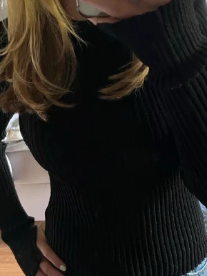 Svart ribbad stickad tröja glittrig  - Säljer en svart ribbad stickad tröja med lång ärm och hög hals. Tröjan har en tight passform och är perfekt för lager på lager under höst och vinter. Enkel och stilren design som passar till allt.