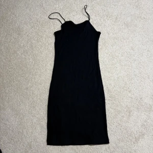 Svart ribbad klänning från BikBok - Svart ribbad klänning från BikBok i storlek S. Klänningen har smala axelband och en tight passform som framhäver siluetten. Enkel och stilren design som är lätt att styla med accessoarer. Perfekt för dig som gillar minimalistisk stil.