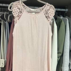 Ljusrosa linnetopp med spetsdetaljer - Snygg ljusrosa linnetopp med spetsdetaljer i blommönster över axlarna. Har ett flowy fall. Aldrig använd, endast testad!