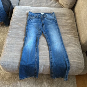 Blå bootcut jeans med fickdetaljer - Snygga blå jeans med bootcut-modell och coola fickor med lock och knapp bak. Jeansen har klassisk tvättad look och sitter skönt i midjan. Perfekta för dig som gillar en avslappnad men ändå trendig stil.
