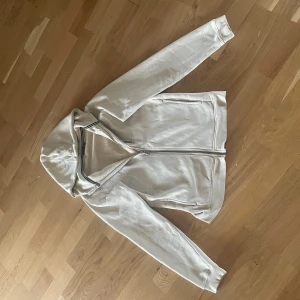 Beige hoodie från Sail Racing med dragkedja - Snygg beige hoodie från Sail Racing med hel dragkedja och broderad logga på bröstet. Tröjan har huva, lång ärm och mjukt fleecefoder på insidan. Perfekt för kyliga dagar och enkel att matcha med ett par jeans. Storlek 176 men motsvarar S. Jag är 183cm lång och precis börjat bli lite för liten på mig.