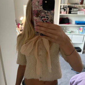 Super söt stickad blus med rosett från Zara💞 - Superfin beige stickad blus från Zara med korta ärmar och stora knappar framtill. Söt och stor rosett i ljusrosa vid halsen som ger en gullig touch. Croppad modell som passar perfekt till jeans eller kjol. Mindre än normalt i storleken så sitter som S!💞 Säljer pågrund av att den inte kommer gilla användning 