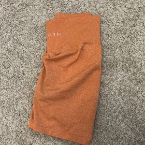 Orange träning shorts från NVGTN - Snygga orangea shorts från NVGTN med hög midja och ribbad linning. Materialet är stretchigt och mjukt, perfekt för gymmet eller andra sportaktiviteter. De har en scrunch-detalj bak för extra passform och stil. Färgen är en fräsch orange ton som sticker ut.