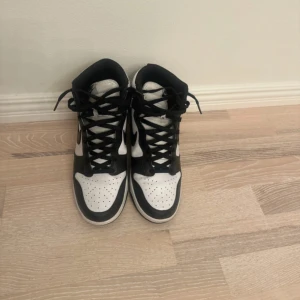 Nike Dunk High svartvita sneakers - Säljer ett par Nike Dunk High sneakers i svart och vitt. Klassisk siluett med högt skaft, svart swoosh och snörning framtill. Ovandel i skinn med perforerad tå för extra ventilation. Perfekta för dig som gillar streetstyle och vill ha en ikonisk look.