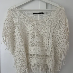 Vit virkad blus med fransar från Zara - Superfin vit virkad blus från Zara Trafaluc med snygga virkade mönster och fransar längs nederkanten och ärmarna. Blusen har en lös passform och är perfekt för sommarens alla tillfällen. Materialet är bomull och den har korta ärmar.