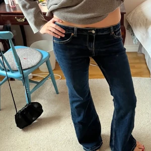 Mörkblå bootcut jeans låg midja - Snygga mörkblå jeans med bootcut passform och låg midja. Klassisk femficksmodell med kontrastsömmar och dragkedja. Perfekta för dig som gillar en retro vibe och vill ha ett par jeans som sitter skönt över höfterna.