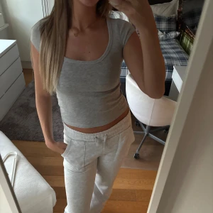 Grå croppad t-shirt med kort ärm - Säljer en enkel och stilren ljusgrå croppad t-shirt med rund halsringning och korta ärmar. Toppen är figurnära och passar perfekt till ett par mjukisbyxor eller jeans. Supermjuk och skön att ha på sig.