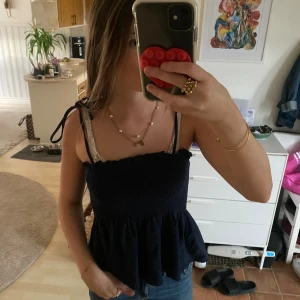 Mörkblå smockad linnetopp med knyt - Supersöt mörkblå linnetopp med smockad överdel och volang nertill. Axelbanden knyts på axlarna för en personlig touch. Perfekt till jeans eller kjol för en chill och trendig look.