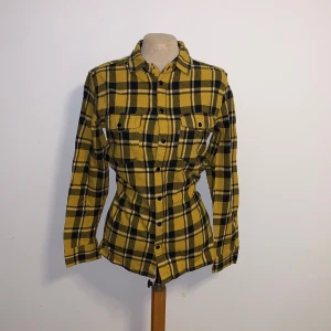 Gul och svart rutig skjorta Good For Nothing - Gul och svart rutig skjorta från Good For Nothing i mjuk bomull. Skjortan har klassisk krage, två bröstfickor med lock och knappar framtill. Perfekt för dig som gillar streetstyle och vill sticka ut med färg. Saknar tyvärr en knapp (de bild)