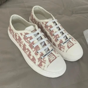 Walk n dior - Snygga sneakers från Christian Dior i rosa och vitt med ikoniskt monogrammönster. Skorna har vit platt sula, rund tå och vita snören. Ovandelen är i textil med broderad logga och detaljer. Perfekta för dig som vill sticka ut med lyxig streetstyle.
