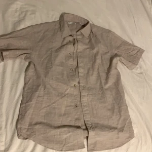 Beige kortärmad skjorta Jack & Jones - Säljer en stilren beige skjorta från Jack & Jones i storlek S. Skjortan är kortärmad med klassisk krage och knappar framtill. Tillverkad i ett lätt och luftigt linnematerial, perfekt för varmare dagar. Enkel och clean look som passar till det mesta.