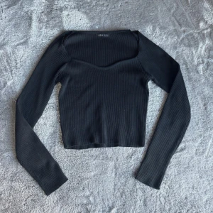Svart ribbad  långärmad  - Snygg svart croppad topp med lång ärm och ribbad struktur. Toppen har en lätt v-ringad halsringning och är perfekt att styla med vad som helst. 