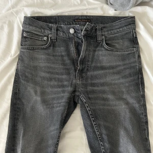 Nudie Jeans, Lean Dean W27 L28 - Snygga grå jeans från Nudie Jeans med klassisk femficksdesign och dragkedja. Jeansen har raka ben och subtila slitningar/tvätt för en cool look. Tillverkade i mjukt bomullstyg och passar perfekt till en avslappnad stil.