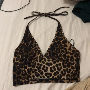 Leopardmönstrad topp  från SHEIN - Snygg topp  från SHEIN i leopardmönster med bruna och svarta toner. Modellen har v-ringad hals och knyt i nacken för justerbar passform. Materialet är mjukt och stretchigt syntet, perfekt för utekväll. Passar dig som vill sticka ut med djurprint i sommar.
