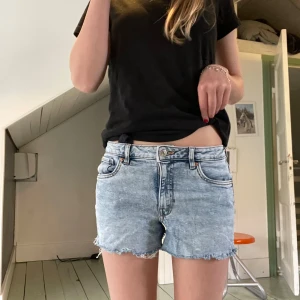Ljusblå jeansshorts med rå kant - Säljer ett par ljusblå jeansshorts från Only med fransig, rå kant och klassisk femficksdesign. Shortsen har låg midja, knapp och dragkedja framtill samt slitna detaljer. De är inte riktigt i min stil och säljer de därför 