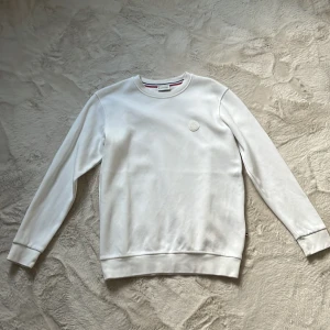 Vit Moncler sweatshirt i bomull - Snygg vit sweatshirt från Moncler med diskret logotyp på bröstet. Tröjan har rund halsringning, långa ärmar och är tillverkad i mjuk bomull. Perfekt för en clean och stilren look.