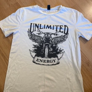 Vit t-shirt med motorcykeltryck från SHEIN - Vit t-shirt från SHEIN med svart tryck av motorcykel, vingar och texten 'UNLIMITED ENERGY' på framsidan. Klassisk rund hals och korta ärmar. Perfekt för dig som gillar coola och unika prints.