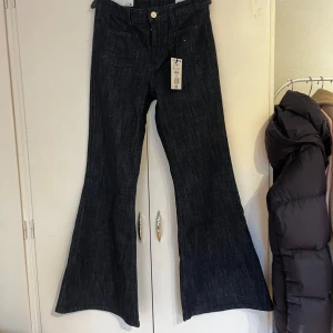 Mörkblå bootcut jeans från Bershka - Snygga mörkblå jeans från Bershka i bootcut-modell med hög midja. Jeansen har klassisk femficksdesign och är tillverkade i ett jeansmaterial som ger en stilren look. Perfekta för dig som vill ha en trendig siluett med extra vidd nertill. Helt nya, så oanvända. Köpta för bara en vecka sedan. Org. Pris 399kr