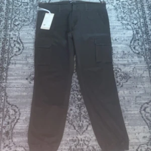 Svarta cargopants - Säljer ett par svarta cargopants från GAS i storlek L. Byxorna har stora fickor på sidorna, resår vid bensluten och är tillverkade i en bomullsblandning med polyester och elastan. Perfekta för en chill och avslappnad look.