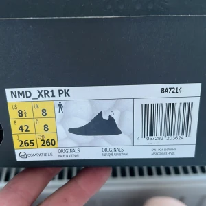 Adidas NMD XR1 PK svarta sneakers - Svarta Adidas NMD XR1 PK sneakers med stickad ovandel i mönstrad design och detaljer i mesh och syntet. Skorna har snörning, platt sula och röda detaljer på hälen. Perfekta för dig som gillar ultraboost osv.