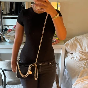Svart axelväska med guldkedja - Säljer en svart axelväska med snygga guldfärgade kedjedetaljer runt kanterna och som axelrem. Stella mccartney liknande!