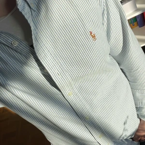 Randig skjorta från Polo Ralph Lauren - Snygg randig skjorta från Polo Ralph Lauren i slim fit. Skjortan är vit med blå ränder, har klassisk krage, knäppning framtill och broderad logga på bröstet. Tillverkad i bomull och passar perfekt till jeans eller chinos. OBS!!!! Osäker på priset så kom med förslag!!!