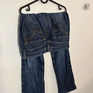 Mörkblå jeans med broderade bakfickor - Snygga mörkblå jeans från FRN i storlek 44. Jeansen har breda ben och coola broderade detaljer på bakfickorna i guld och vitt. Klassisk femficksmodell med kontrastsömmar och en avslappnad vibe. Perfekta för dig som gillar en lite mer unik jeansstil.