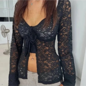 Svart spetsblus från Design by Si - Supersnygg svart blus i spets från Design by Si. Blusen har långa ärmar, v-ringning och knyt framtill. Aldrig använd! Flyttar så vill ha så snabb affär som möjligt