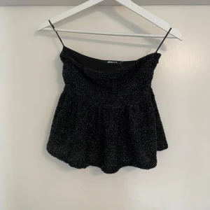 Glittrig svart linnetopp från Gina Tricot - Supersnygg svart glittrig linnetopp från Gina Tricot med lätt utställd passform. Perfekt för att sticka ut med sitt skimrande material och trendiga look. Toppen har en mjuk struktur och är riktigt bekväm att bära.