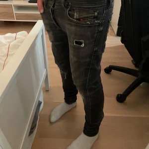 Diesel svarta slitna jeans - Säljer ett par svarta jeans från Diesel med slitningar och hål på framsidan och vid knäna. Nypris: 1800 kr, gjorda slitningar. Knappast andvända jeans. 