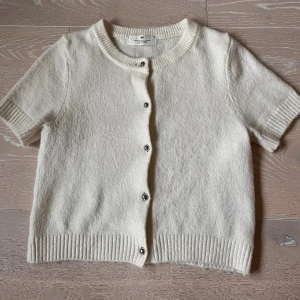 Vit kortärmad kofta från H&M - Superfin vit kofta från H&M i mjuk ullmix. Kortärmad modell med ribbade kanter och rund halsringning. Silvriga knappar framtill. Inte nopprig och skönt material!💋