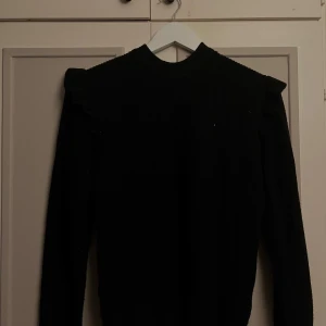 Svart stickad tröja med volanger - Svart stickad tröja från Object i storlek S. Tröjan har lång ärm, ribbad struktur och snygga volangdetaljer vid axlarna. Nästan helt ny! 