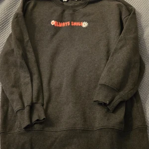 Mörkgrå sweater! - Mysig mörkgrå sweatshirt från Primark med rosa text och blommor på bröstet och ryggen. Texten säger 'Always Smile' och 'Nothing to do today but smile'. Tröjan har långa ärmar och ribbade muddar. Bra till jeans! Eller till mysig tröja hemma! Stl xs men är oversized! Skriv om du är intresserad eller har några frågor! 🫶🌸🍁