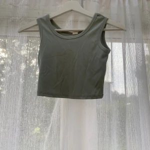 Ljusgrå ribbad linnetopp - Snygg ljusgrå ribbad linnetopp med croppad passform och breda axelband. Toppen har en enkel och stilren look som passar perfekt till jeans eller kjol. Materialet är mjukt och stretchigt för en bekväm känsla.