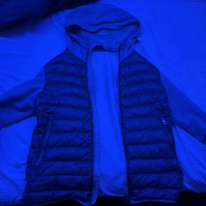 Moncler dunväst med huva, storlek S - Säljer en snygg dunväst från Moncler i storlek S. Jackan har en quiltad design, dragkedja framtill och två sidofickor med dragkedja. Den har en grå huva och är perfekt för lager-på-lager. Klassisk Moncler-stil som funkar året runt. Skicka för mer bilder. Pris kan diskuteras! Självklart äkta!