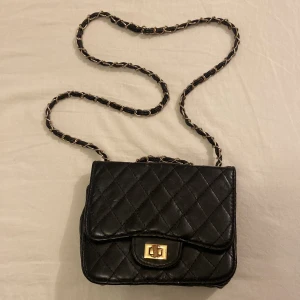 Svart axelväska med kedja - Snygg svart axelväska. Använt flertal gånger. Bra skick. Små defekter och sminkfläckar insidan av väska  (se bilder). 