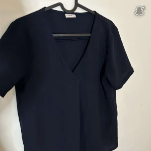 Mörkblå v-ringad topp från JDY - En stilren mörkblå topp från JDY i storlek XS. Toppen har korta ärmar och en djup v-ringning framtill. Enkel och clean design som är lätt att matcha med olika outfits. Perfekt för dig som gillar minimalistisk stil.