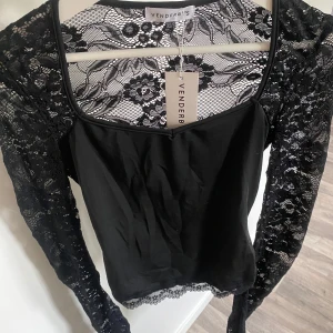 Svart spetsblus från Venderby’s - Supersnygg svart blus från Venderby’s med långa ärmar i genombruten spets och blommigt mönster. Toppen har en tight passform, fyrkantig ringning och fina spetsdetaljer vid nederkanten. Perfekt för dig som vill sticka ut lite extra.