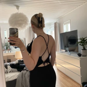 Svart ribbad klänning med öppen rygg - Säljer en svart ribbad klänning i storlek M med smala axelband som korsas i ryggen och knyts nedtill. Klänningen är ärmlös, har en tight passform och öppen rygg vilket ger en snygg och modern look. Perfekt för dig som gillar minimalistisk stil.