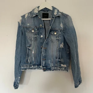 Distressed jeansjacka från Zara - Snygg ljusblå jeansjacka från Zara i storlek M med slitna detaljer. Klassisk modell med bröstfickor, knappar framtill och coolt vintage-vibe. Sparsamt använd! 