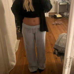 Ljusgrå stickade byxor med snörning - Säljer ett par ljusgrå stickade byxor med snyggt hålmönster och breda ben. Byxorna har hög midja och dragsko i midjan för extra komfort. Perfekta för en chill och trendig look.