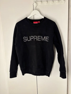 Svart Supreme sweatshirt i bomull - Supreme crewneck i svart med stor vit broderad logga över bröstet. Klassisk rund hals och ribbade muddar vid ärmslut och nederkant. Tillverkad i Kanada, mjuk bomullskvalitet som är skön att bära. Perfekt för dig som gillar streetwear och vill sticka ut. Har använts fåtal gånger. Tveka inte på att skriva ett prisförslag.