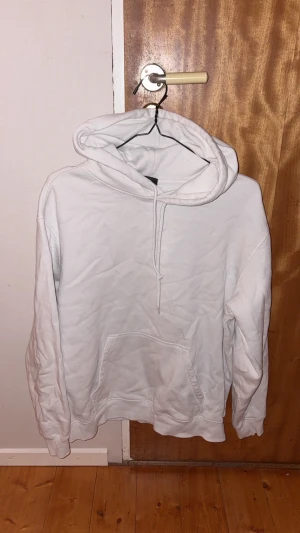 Vit hoodie med huva och ficka - Säljer en enkel vit hoodie med stor huva och snörning. Tröjan har en klassisk känguruficka framtill och långa ärmar. Perfekt för chill dagar och passar till det mesta. Mjuk och skön känsla tack vare bomullsmaterialet.