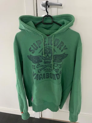 Grön Superdry hoodie  - Snygg grön hoodie från Superdry i storlek M, modellen är ca 180cm. Hör av dig vid funderingar!